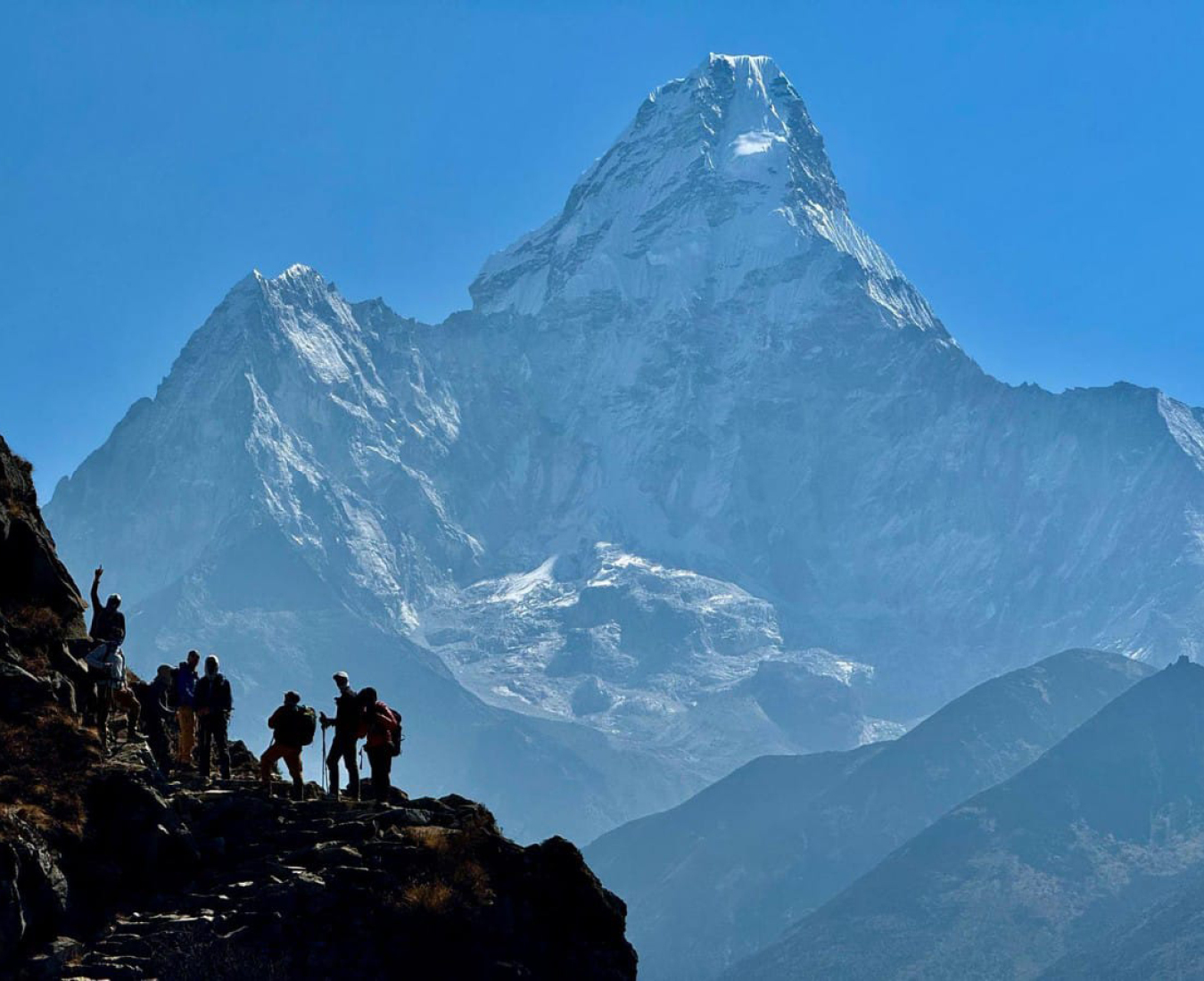 Trekkers overshadowed by the immense profile of Mount Ama Dablam on the trail.
